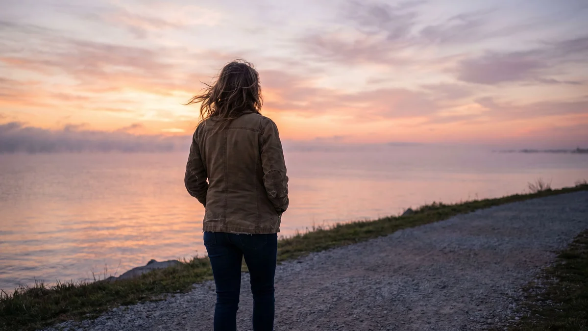 A woman walking on a lakeshore path at sunrise